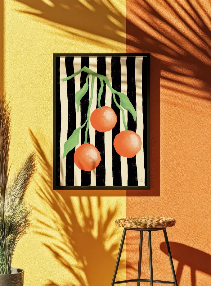 “Citrus Pop” art print by Spektaklet Studio – oranges on striped black-and-white background, framed and hanging on a colorful yellow-orange wall in sunlight.